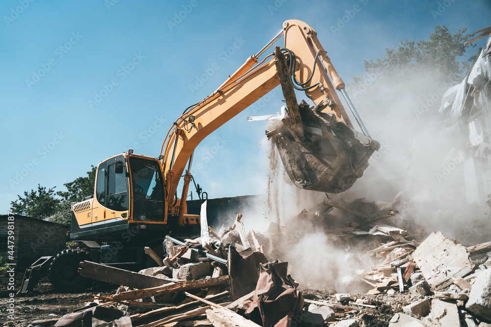 Destruction of old house by excavator. Bucket of excavator breaks concrete structure.